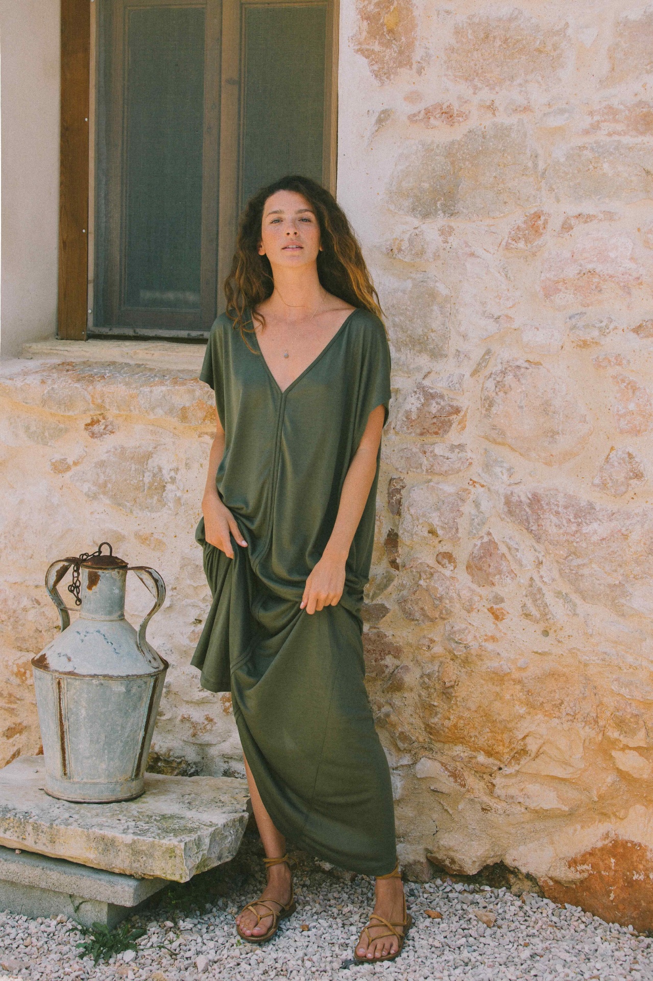 AWAN olive draped dress by a rustic stone wall