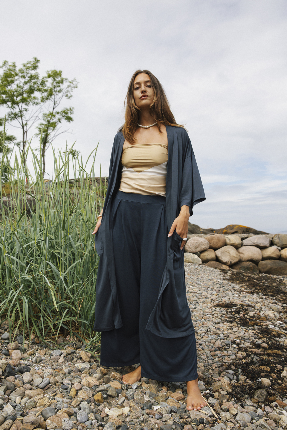 AWAN deep blue cardigan and trousers on a pebbled coast